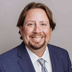 Headshot of Quinton L. Clayton smiling in a blue suit jacket and tie.